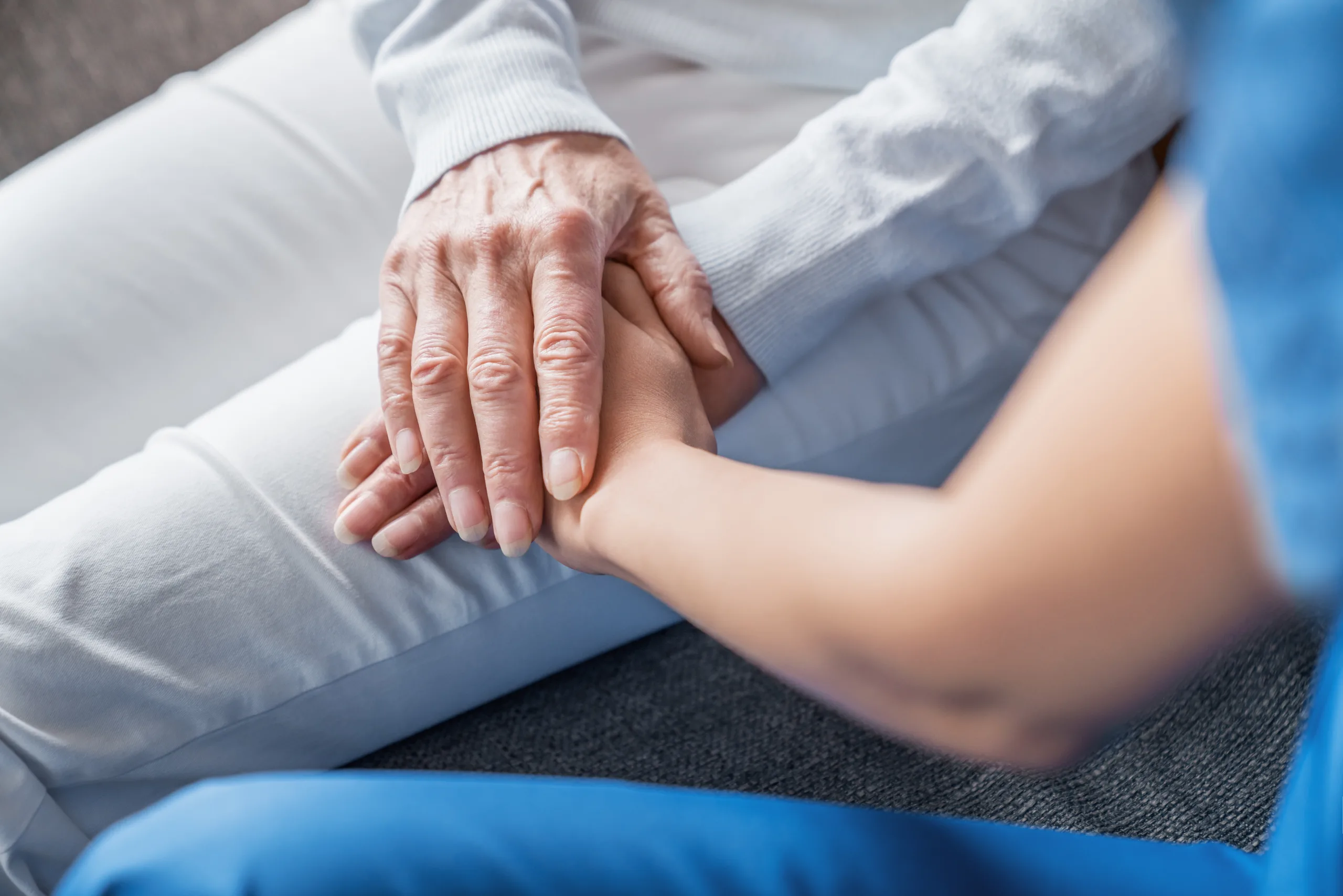 Close up image of caregiver holding hands of elderly patient during home visit