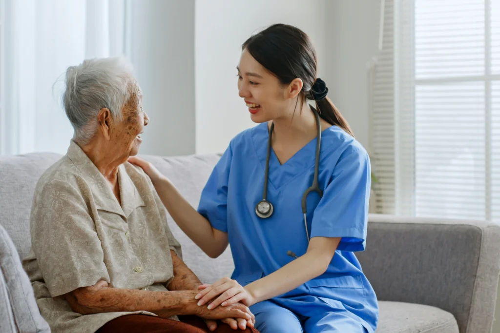 Home health aide and elderly client sharing a friendly moment on a couch during an in-home care visit